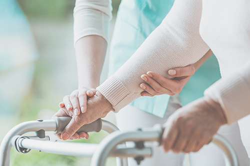 Close of up elderly woman's hand on a walker being assisted by nurses hands